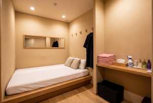 部屋の中央にシングルベッド1台、木のフレームと白いリネンを配した、ミニマルなデザイン...。