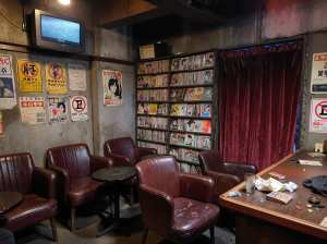 ヴィンテージ感のある薄暗い部屋で、手前に赤い革張りの椅子と木製のテーブルが置かれています。