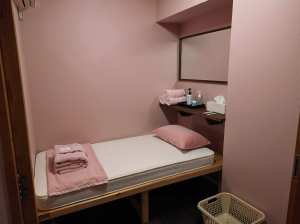 ピンクの壁と中央にシングルベッドが置かれたミニマルなベッドルーム。