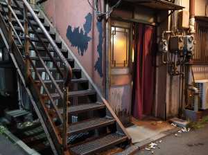 ローアングルから写実的に撮影したもので、青いペンキが剥がれ落ちた老朽化した建物に続く...。