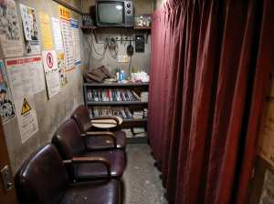 薄暗い部屋の右側に赤いカーテンがあり、壁にはポスターが貼られています。