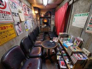 薄暗い部屋の中央に小さなテーブルがあり、その周りには空の椅子が置かれている。