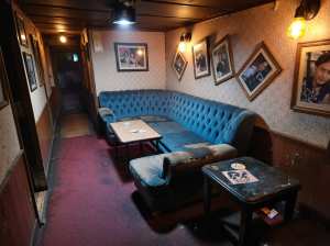 薄暗い部屋の中央に青いベルベットのチェスターフィールドソファがあり、その両側に小さな...。