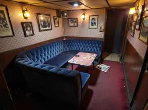 薄暗い部屋の中央に青いベルベットのセクショナルソファと小さなピンクのテーブルが置かれ...。