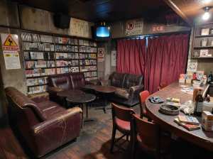 素朴でヴィンテージな雰囲気の薄暗い部屋で、木の床と壁にはポスターや思い出の品が飾られ...。