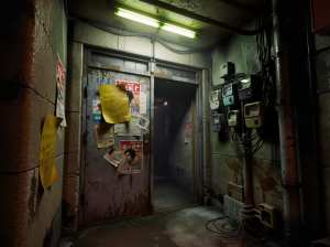 薄暗く、錆びた金属のドアとポスターが貼られたインダストリアルな廊下。