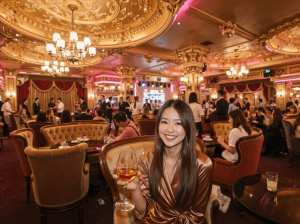 高級レストランに座ってコニャックのグラスを持ち、カメラに向かって微笑む女性を正面カメ...。