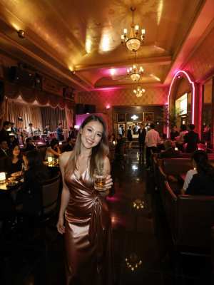 高級レストランでビールのグラスを持ち、カメラに向かって微笑む女性を正面から写実的に撮...。