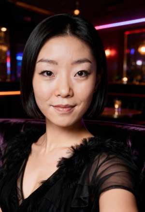 カラフルなライトを背景に薄暗い部屋に座っている、黒い薄手のドレスを着て毛皮のストール...。