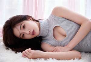 ふわふわの白い敷物の上に横たわり、カットアウトデザインのグレーのニットノースリーブト...。