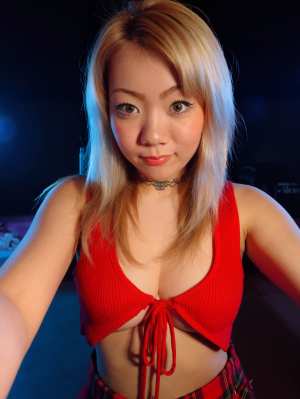 赤いクロップトップとチェック柄のスカートを着て自撮りをする若い女性を自撮りアングルか...。