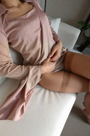 モダンなリビング ルームの白いソファに座り、淡いピンクの長袖ドレスとサイハイ ストッ...。