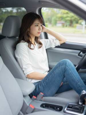 車の運転席に座って思慮深い表情をしている若い女性を横から撮った写実的な写真。