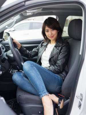 黒い革のジャケットとブルー ジーンズを着て、現代の車の運転席に座っている若い女性を横...。