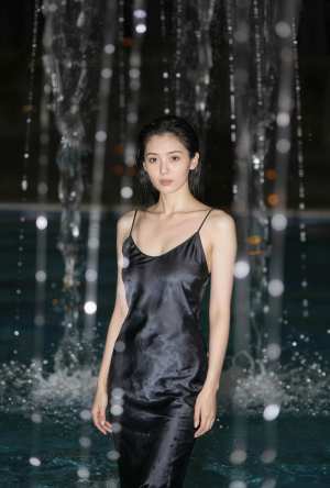 絹のような黒いスリップ ドレスを着て、夜の噴水の前に立つ若い女性を正面カメラ アング...。