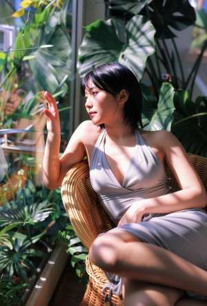 屋内で、豊かな緑に囲まれた籐の椅子に座っている若い女性を横顔カメラのアングルから写実...。