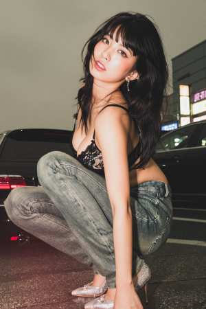 黒いレースのブラジャーとジーンズを着て、夜の街路でしゃがむ若い女性を横から撮影した写...。