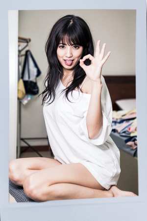 楽屋のベッドに座り、右手で「OK」のジェスチャーをしている若い女性のポラロイド写真。