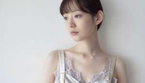 真っ白な壁を背景に撮影された、中性的な表情を持つ若い女性の写実的なポートレート。