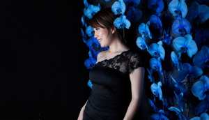 黒いドレスを着て、青い蘭の花の壁の前に立つ若い女性を横顔カメラのアングルから写実的に...。