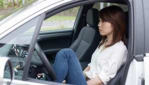 現代の車の運転席に座り、瞑想的な表情で窓の外を眺めているアジア系の若い女性。