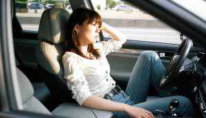 白いブラウスとブルー ジーンズを着て、現代の車の運転席に座っている若い女性を横から撮...。