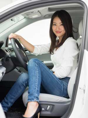 現代の車の運転席に座り、ハンドルを握りながら自信に満ちた笑みを浮かべているアジア系の...。