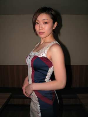 中間色の壁と木製パネルを背景にした薄暗い部屋に立つアジア系の若い女性の写実的なポートレート。