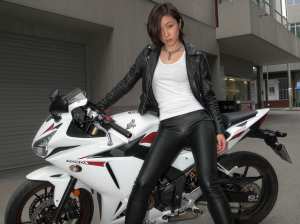 都市部でバイクの隣でポーズをとる若い女性を横から撮った写実的な写真。