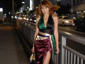 ぼやけた街の明かりを背景に、ファッショナブルな服装をした女性が夜の歩道を歩く様子をサ...。