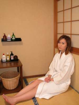 スパのような環境でマットに座っている白いバスローブを着た若い女性を横から撮影したリア...。