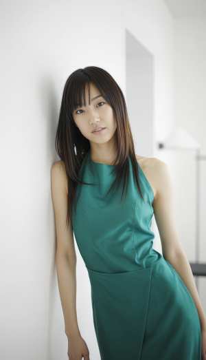 壁にもたれかかり、中立的な表情でカメラを直接見つめている、ティール色のドレスを着た若...。