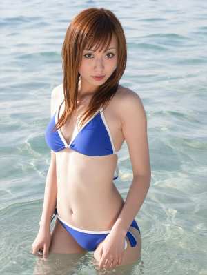 ビーチの浅瀬に立っている青いビキニを着た若い女性を、正面カメラのアングルから写実的に...。