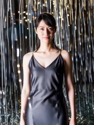 シルクのようなグレーのスリップ ドレスを着て、吊り下げられたライトの背景の前に立つ若...。