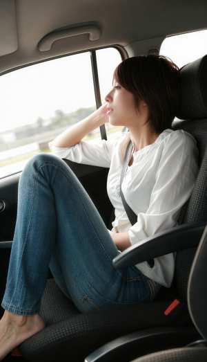 白いブラウスとブルー ジーンズを着て、車の中で座って思索にふける若い女性を横から撮っ...。