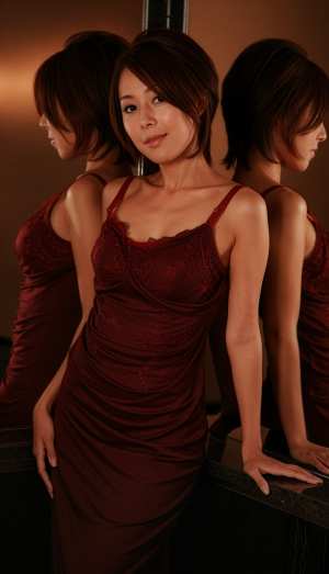 赤いドレスを着て鏡の前に立ち、自信に満ちた表情で自分を見つめる女性を横顔カメラのアン...。