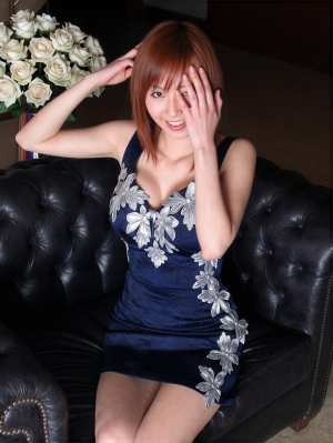 白いバラの花束を背景に、黒い革張りのソファに座っている若い女性を正面から写実的に撮影...。