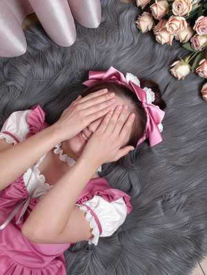 白いレースのトリムが付いたピンクのドレスを着て、髪にピンクのリボンを付けた若い女性が...。