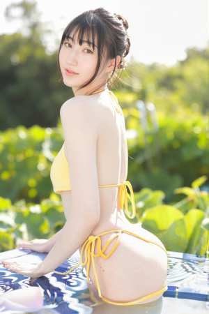 緑に囲まれたプールサイドでポーズをとっている黄色いビキニを着た若い女性を横から撮った...。