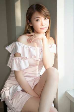 フリルの付いたピンクのオフショルダー ドレスを着て、明るい色の部屋で壁に向かって座っ...。