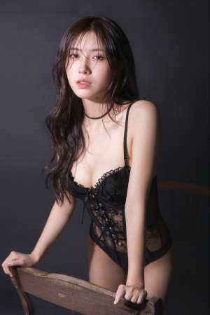 黒いレースのランジェリーセットを着て木製の椅子にもたれてポーズをとる若い女性を、ポー...。