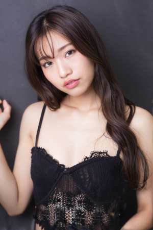 レースのディテールが施された薄手の黒いトップスを着て、暗い背景に自信を持ってポーズを...。