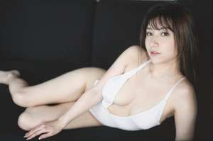 白いタンクトップを着た若い女性が黒い地面に座り、真剣な表情でカメラを見つめている様子...。