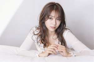 柔らかい中間色の部屋の白いベッドに横たわる、長くウェーブのかかった茶色の髪を持つ若い...。