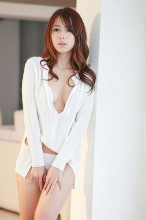 ミニマルな屋内環境で、白い壁に向かって自信を持ってポーズをとる若い女性を横から撮った...。