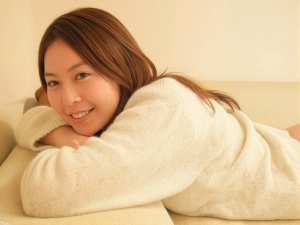 ベージュのソファに横たわり、カメラに向かって微笑む若い女性の写実的なポートレート。