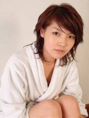 白いバスローブを着て、リラックスしたポーズで木の表面に座っているアジアの若い女性の写...。