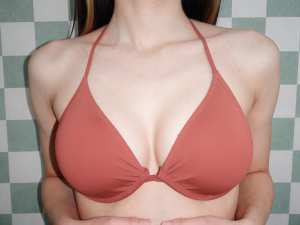 緑と白の市松模様の背景にサンゴ色のビキニトップを着た女性を正面カメラのアングルから写...。