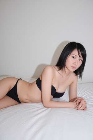 ミニマルな寝室の設定で、ベッドの上でポーズをとる若い女性を横から見た写真のようにリア...。