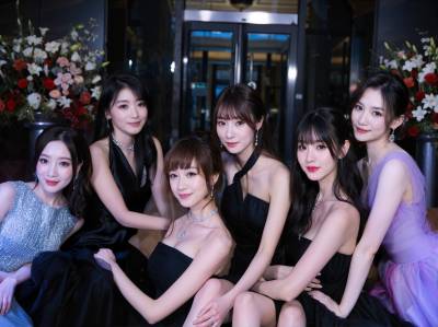 花で飾られた豪華なロビーの前で写真を撮る 7 人の若い女性のグループ。